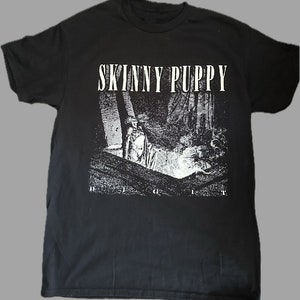 Może przedstawiać: Czarny T-shirt z białym nadrukiem graficznym zespołu "Skinny Puppy". Grafika przedstawia czarno-biały obraz osoby w ciemnym otoczeniu.