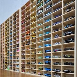 May include: Two tall, light-coloured wooden display shelves featuring numerous rectangular compartments. Each individual cubby holds a single miniature toy car, showcasing a diverse collection of various models, colours, and designs arranged in rows.