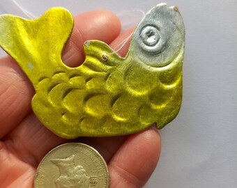 Puede incluir: Un adorno de pescado de metal amarillo y plateado con una cuerda blanca atada. El pez es aproximadamente del tamaño de una moneda de euro.