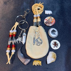 May include: A collection of handmade items with a wolf theme. Includes a small leather pouch, keychains with wolf charms, beaded accents, carved stone figures, and decorative buttons with wolf imagery. The items are arranged on a dark surface.