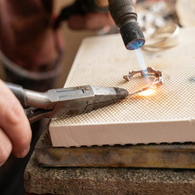 A person is using a blowtorch to heat and shape a piece of metal in a workshop setting.