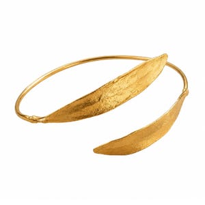 Può includere: Un bracciale aperto color oro caratterizzato da due elementi allungati a forma di foglia con una superficie organica e testurizzata. Il bracciale presenta un sottile cerchio che collega le due forme a foglia appuntite.
