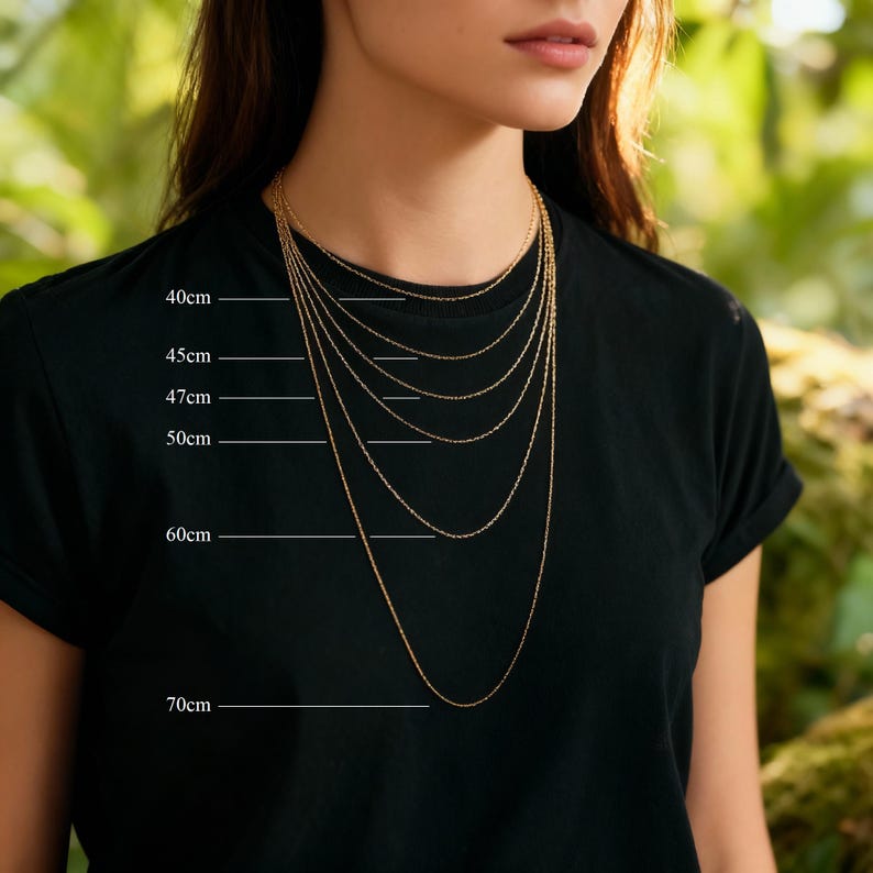 A close-up of a woman wearing a black t-shirt with a gold necklace, and the necklace has multiple chains of varying lengths.