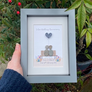 May include: A framed pebble art picture of a couple sitting on a bench with a heart-shaped balloon. The text reads "Silver Wedding Anniversary" and "Eve & Edmond Est 28th February 1993".
