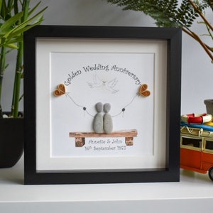 May include: A framed pebble art piece with a couple sitting on a bench. The art is titled "Golden Wedding Anniversary" and includes the names Annette & John and the date 16th September 1972.