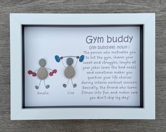 May include: A framed print with a hand-drawn illustration of two people lifting weights. The print includes the text "Gym buddy (jim buhd:ee) noun: The person who motivates you to hit the gym, shares your sweat and struggles, laughs at your jokes (even the bad ones), and sometimes makes you question your life choices during intense workout sessions. Basically, the friend who turns fitness into fun and makes sure you don't skip leg day!" The names "Amelie" and "Lisa" are written below the illustrations.