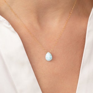 May include: A delicate gold chain necklace with a teardrop-shaped blue gemstone pendant.
