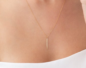 May include: A delicate gold chain necklace with a thin, vertical bar pendant. The bar is set with small, sparkling diamonds.