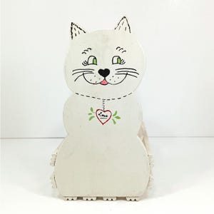 May include: A white ceramic mug with a black handle and the text "But First, Coffee" in a handwritten style. The mug is on a white surface. The mug is approximately 4 inches tall.