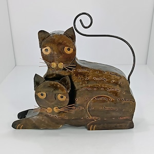 May include: A metal sculpture of two brown cats, one larger than the other, with a curled tail. The cats are stylized with cut-out details and have copper-colored eyes.