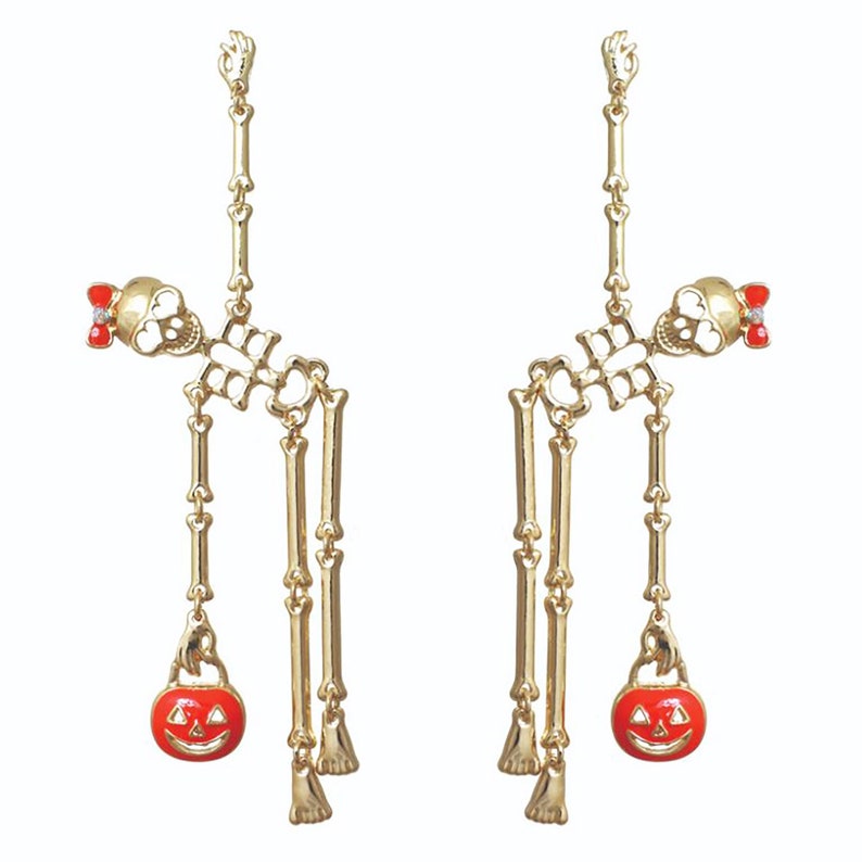 May include: A pair of gold-colored Halloween earrings. Each earring features a skeleton design with a red bow and a dangling orange pumpkin with a carved face. The earrings are designed to dangle.