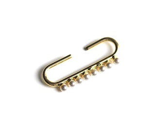May include: A gold-toned ear cuff with a row of small white pearls hanging from the bottom.