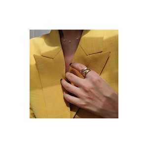 Könnte beinhalten: Ein goldener Ring mit einem strukturierten Design. Der Ring wird am Zeigefinger einer Hand getragen.