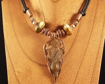 May include: A handmade necklace with a large, pale stone pendant encased in copper wire. It has a black leather cord, copper beads, and natural stone details. The pendant is the centrepiece, highlighting the stone's unique texture and colour.