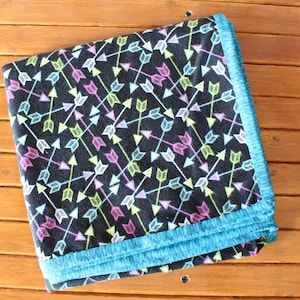 May include: A black fleece blanket with a turquoise border. The blanket has a repeating pattern of colorful arrows.