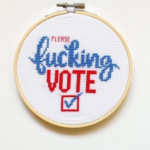 Może przedstawiać: Haft krzyżykowy w drewnianej tamborku z napisem "PLEASE fucking VOTE" w niebieskiej i czerwonej nici. Znak wyboru znajduje się w czerwonym kwadracie. Tło jest białe.