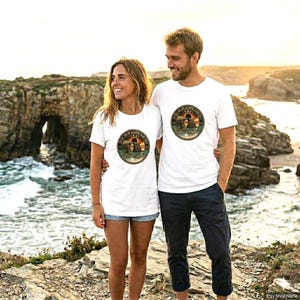 Op de afbeelding: Een wit T-shirt met korte mouwen en een ronde afbeelding op de borst. De afbeelding toont een rotsboog aan de kust bij zonsondergang met de tekst "DURDLE DOOR" en "Golden Spirit" gedrukt in een cirkelvormige rand eromheen.