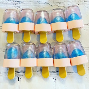 May include: Ten clear plastic popsicle-shaped containers with blue liquid inside. The containers are topped with a pink lid and have a white stick.