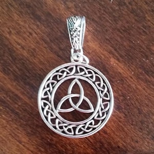May include: Silver pendant featuring a Celtic knot design with a circular frame. The pendant has a detailed, intricate design.