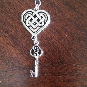 May include: Silver pendant necklace featuring a heart-shaped Celtic knot design with a key charm hanging below.