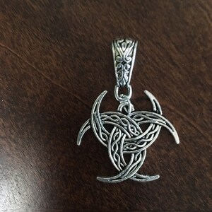 May include: Silver pendant with a triple moon design. The pendant is made of metal and has a Celtic knot pattern.