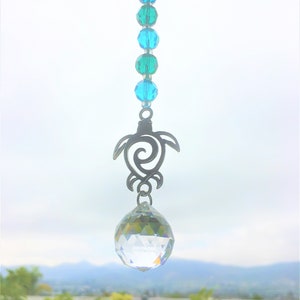 May include: A crystal suncatcher with a silver turtle charm and a string of turquoise and blue beads hanging from a window.