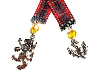 May include: Two bookmarks with red and green tartan ribbon. Each has a silver charm, one a lion, the other a thistle. Yellow crystal beads dangle below.