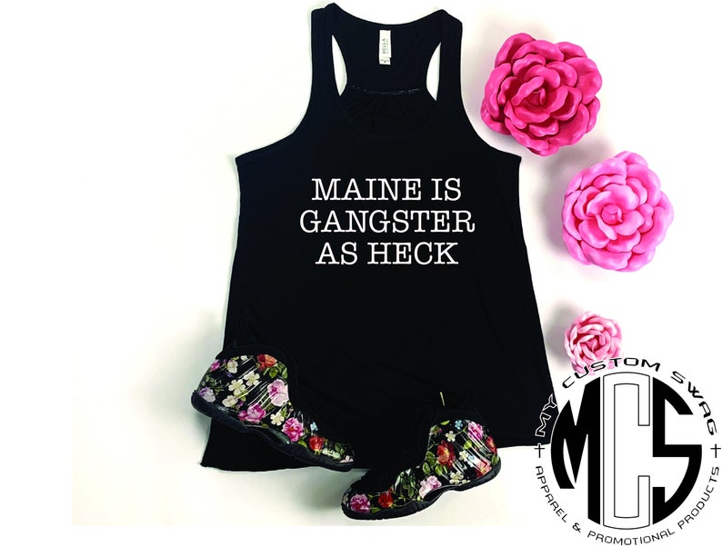 May include: Black tank top with the text "MAINE IS GANGSTER AS HECK" in white. The image also features floral print sneakers and pink flowers. The logo for "MY CUSTOM SWAG + APPAREL & PROMOTIONAL PRODUCTS" is in the lower right corner.