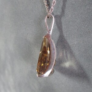 Peut inclure: Un collier avec un pendentif en argent et une pierre pr&eacute;cieuse de couleur brun clair, de forme goutte d'eau et facet&eacute;e.