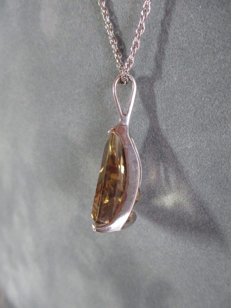 Peut inclure: Un collier avec un pendentif en argent et une pierre pr&eacute;cieuse de couleur brun clair, de forme goutte d'eau et facet&eacute;e.