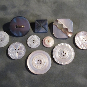 May include: Assortment of 10 vintage buttons in various shapes, sizes, and colors. The buttons are made of mother of pearl, plastic, and metal. Some buttons have intricate designs, while others are plain.