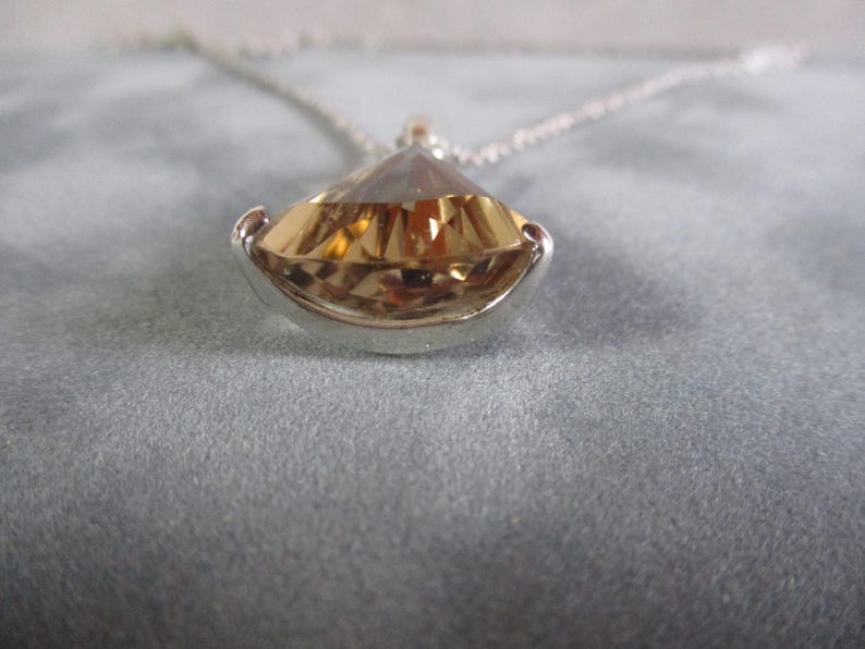 Peut inclure: Un collier en argent avec un grand pendentif en forme de larme facett&eacute;, transparent. Le pendentif est de couleur or et est serti dans une b&eacute;li&egrave;re en argent.
