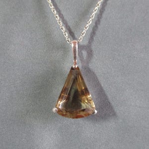Peut inclure: Un collier en cha&icirc;ne argent avec un pendentif en forme de larme orn&eacute; d'une pierre pr&eacute;cieuse brune et verte.