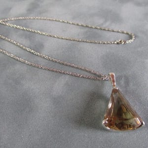 Peut inclure: Un collier en cha&icirc;ne argent avec un pendentif orn&eacute; d'une grande pierre pr&eacute;cieuse brune facet&eacute;e. Le pendentif a la forme d'une larme.