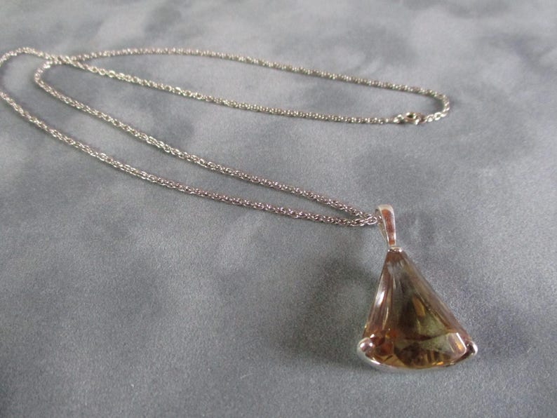 Peut inclure: Un collier en cha&icirc;ne argent avec un pendentif orn&eacute; d'une grande pierre pr&eacute;cieuse brune facet&eacute;e. Le pendentif a la forme d'une larme.