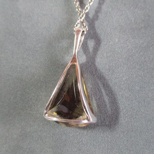 Peut inclure: Un collier avec un pendentif en argent et une pierre pr&eacute;cieuse de forme triangulaire. La pierre pr&eacute;cieuse est de couleur brun clair et a une taille facet&eacute;e.