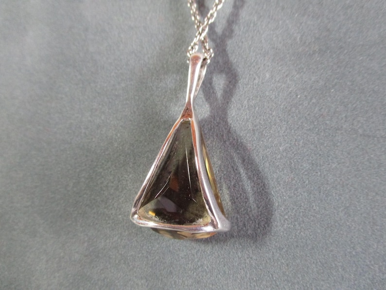 Peut inclure: Un collier avec un pendentif en argent et une pierre pr&eacute;cieuse de forme triangulaire. La pierre pr&eacute;cieuse est de couleur brun clair et a une taille facet&eacute;e.