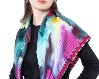 May include: A woman wearing a black long-sleeved shirt with a colorful patterned scarf. The scarf has a pink, purple, blue, green, and yellow watercolor design with a white and black houndstooth border.