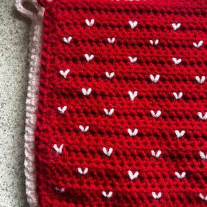 May include: Red crochet potholder with white heart accents. A light pink crochet potholder is layered underneath. The potholders have a loop for hanging. Handmade kitchen decor.