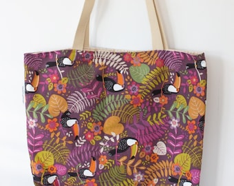 Può includere: Una borsa tote viola con una stampa colorata di tucani e fiori. La borsa ha due lunghe cinghie beige.