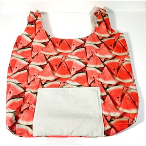 May include: A red and green reusable tote bag with a watermelon print. The bag has a large pocket on the front.