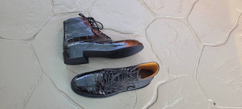 May include: Two pairs of black leather ankle boots with crocodile print. The boots have laces and a chunky heel.