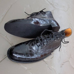 May include: A pair of black leather boots with a crocodile pattern. The boots have laces and a rounded toe.