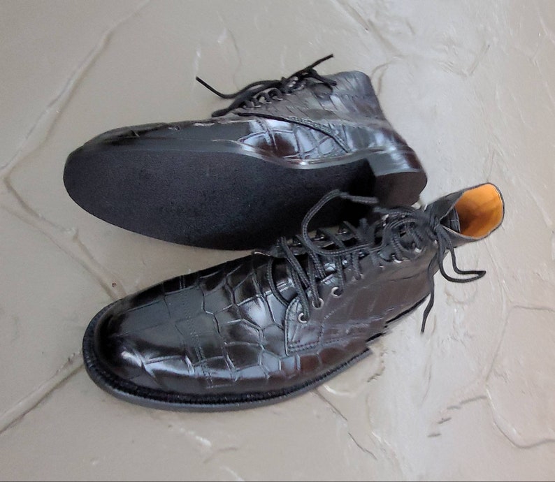 May include: A pair of black leather boots with a crocodile pattern. The boots have laces and a rounded toe.