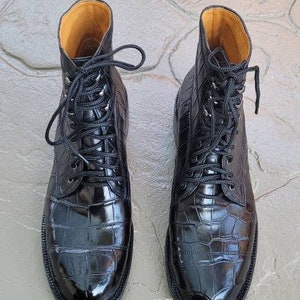 May include: A pair of black leather boots with a crocodile pattern. The boots have laces and a pointed toe.