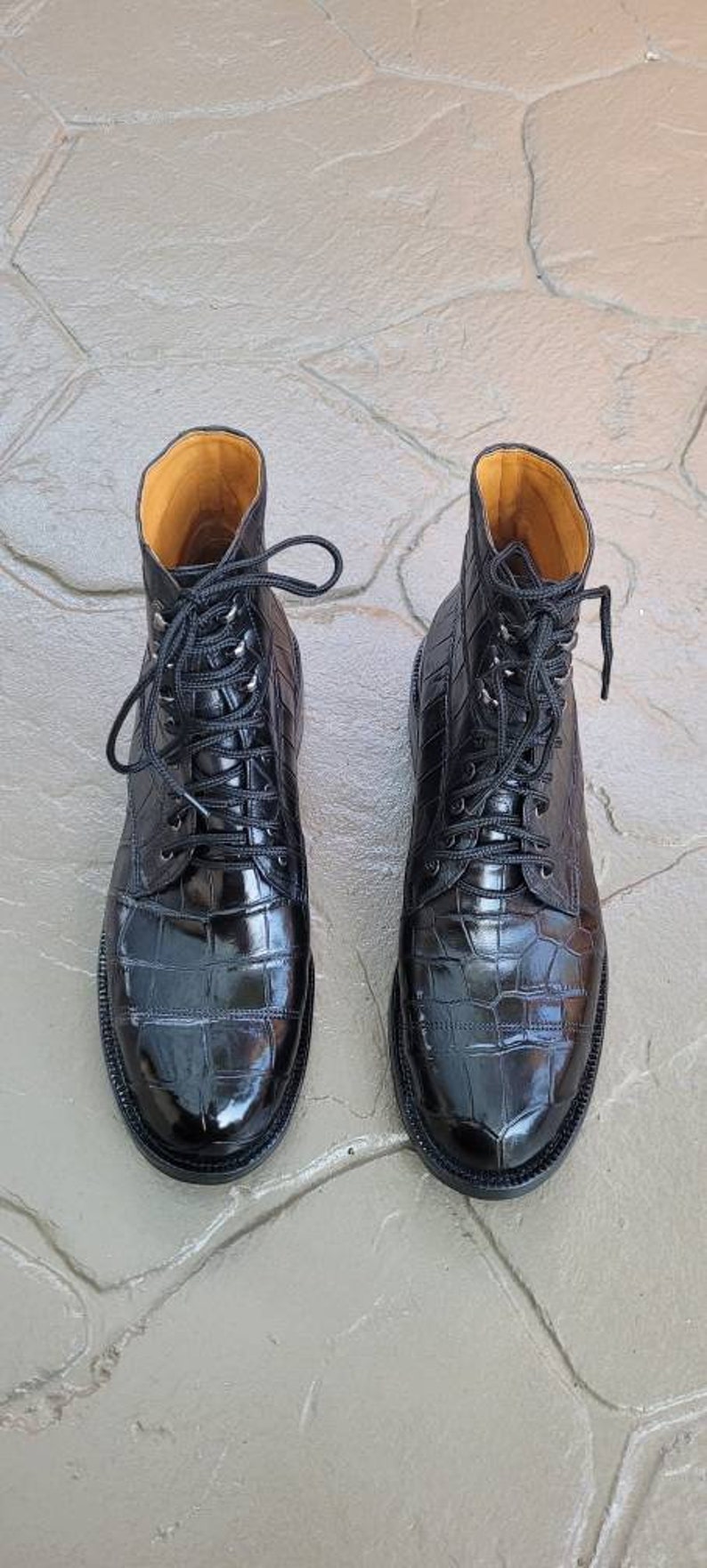 May include: A pair of black leather boots with a crocodile pattern. The boots have laces and a pointed toe.