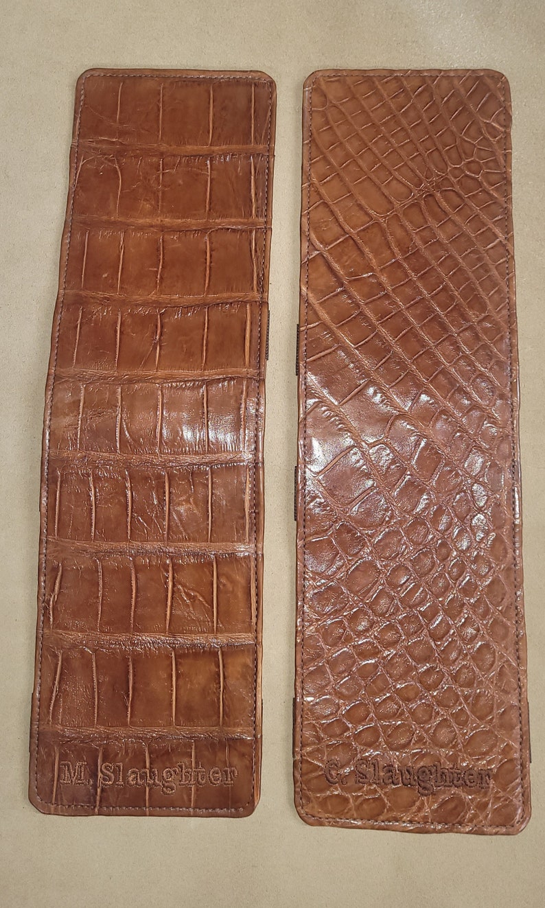 Puede incluir: Dos carteras de cuero marr&oacute;n con patrones de piel de cocodrilo. Las carteras est&aacute;n grabadas con el texto "M. Slaughter" y "G. Slaughter".