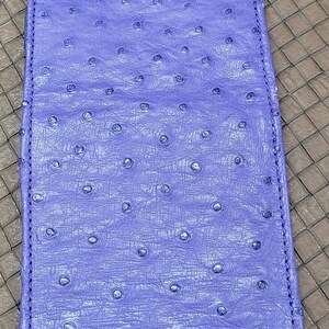 Puede incluir: Una cartera de piel de avestruz de color morado con las iniciales "REPC" bordadas en hilo azul.