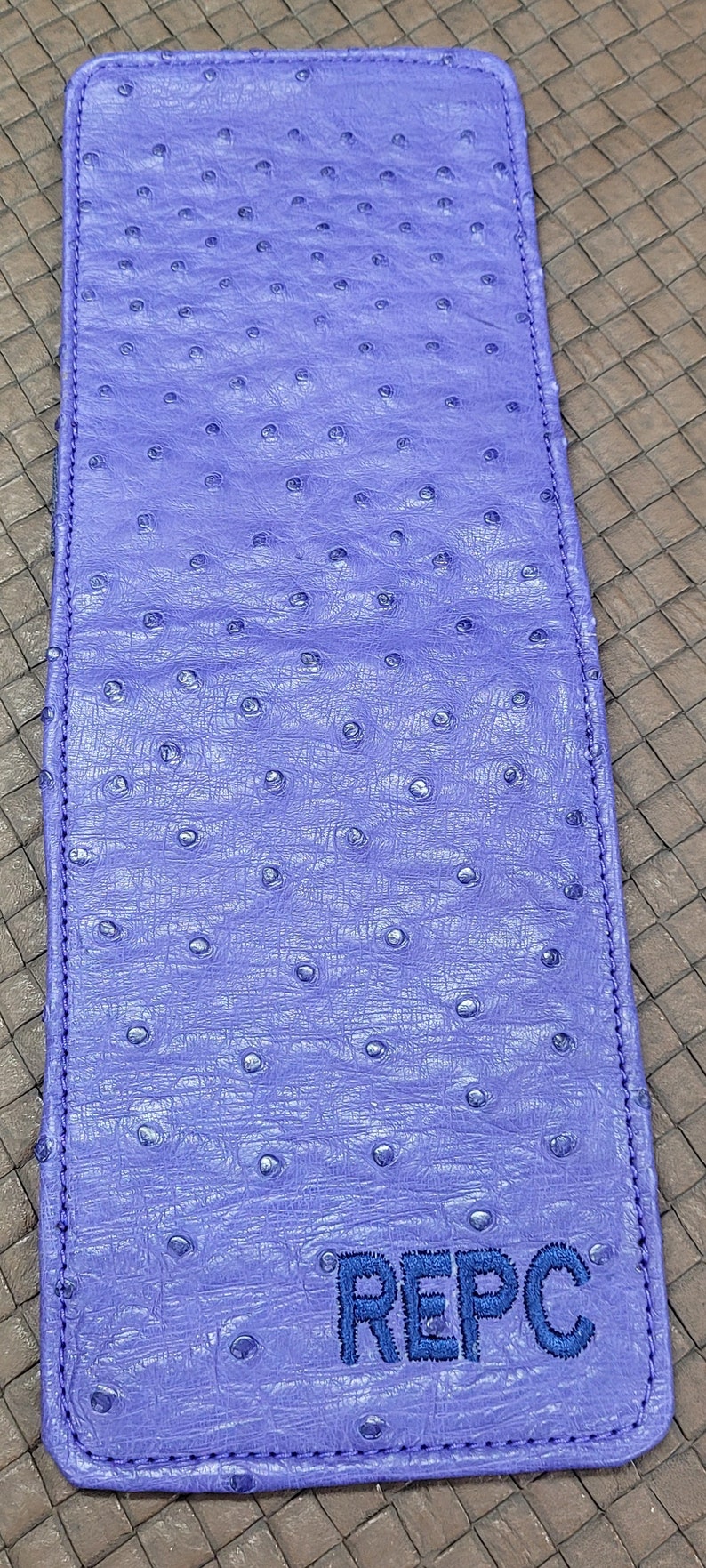 Puede incluir: Una cartera de piel de avestruz de color morado con las iniciales "REPC" bordadas en hilo azul.