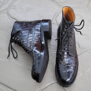 May include: A pair of black leather lace-up boots with a crocodile pattern. The boots have a pointed toe and a chunky heel.